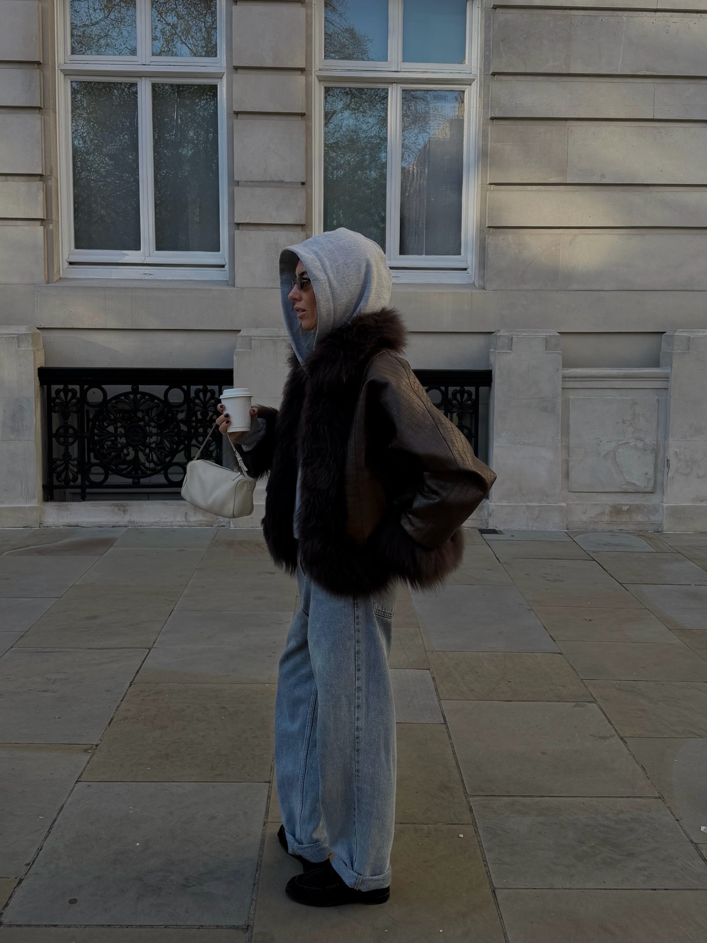 Hannah wears a gray sweatshirt, fur-trimmed coat, baggy jeans, and loafers.