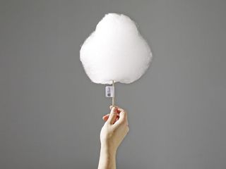 A caucasian hand holding up a white wool-like cotton candy . Photographed against a grey background