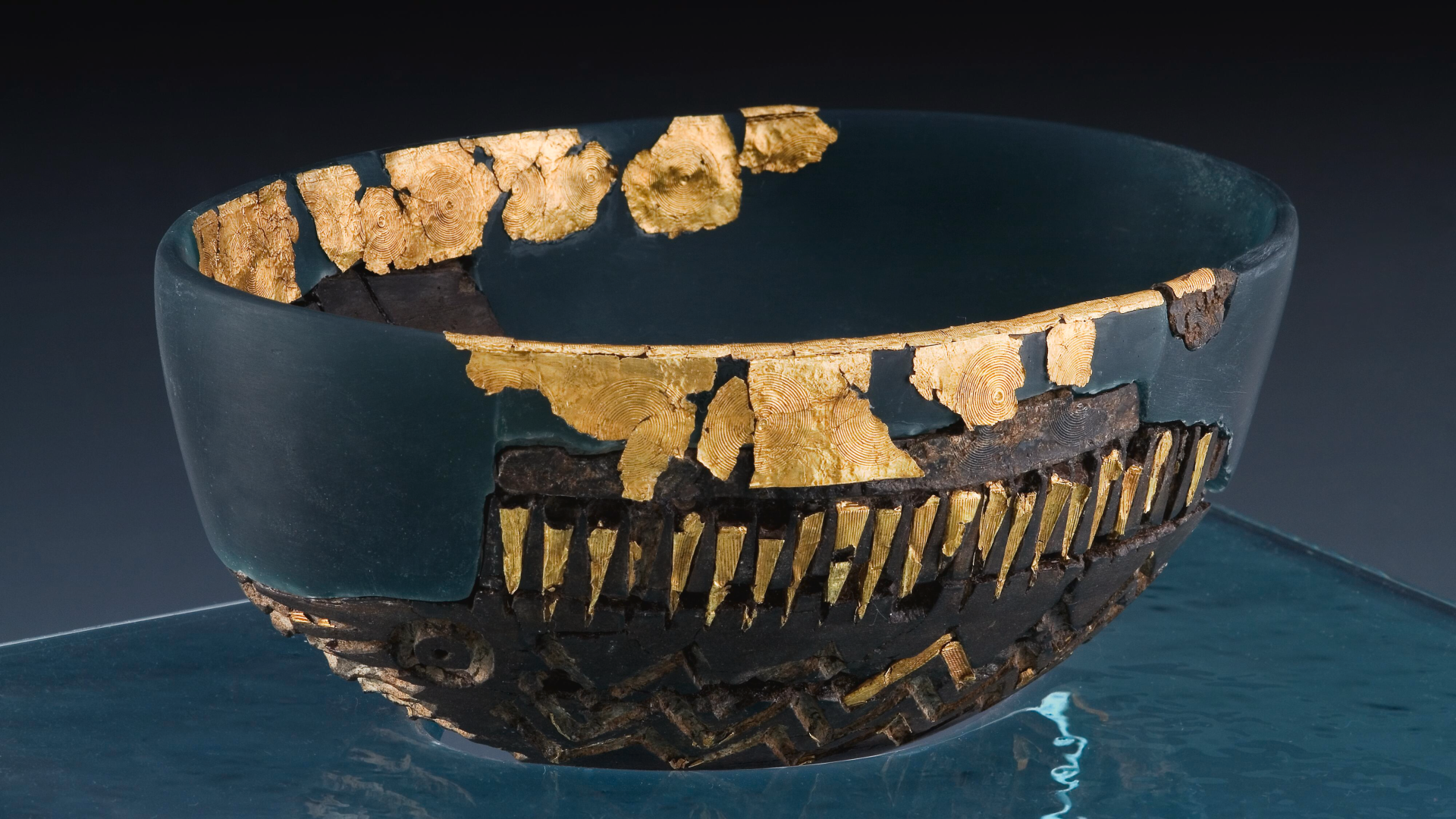a fragmentary dark teal colored bowl has accents of gold lines, circles and zigzags