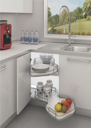 Kidney shaped pull-out shelves emerging from an open corner cabinet in a white kitchen.