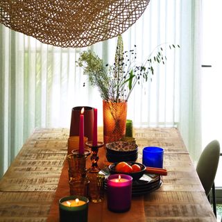 a dining table setting with coloured glassware and crockery and a low pendant light