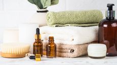 Some folded towels surrounded by essential oil dropper bottles, a pump bottle, and natural bamboo body brushes