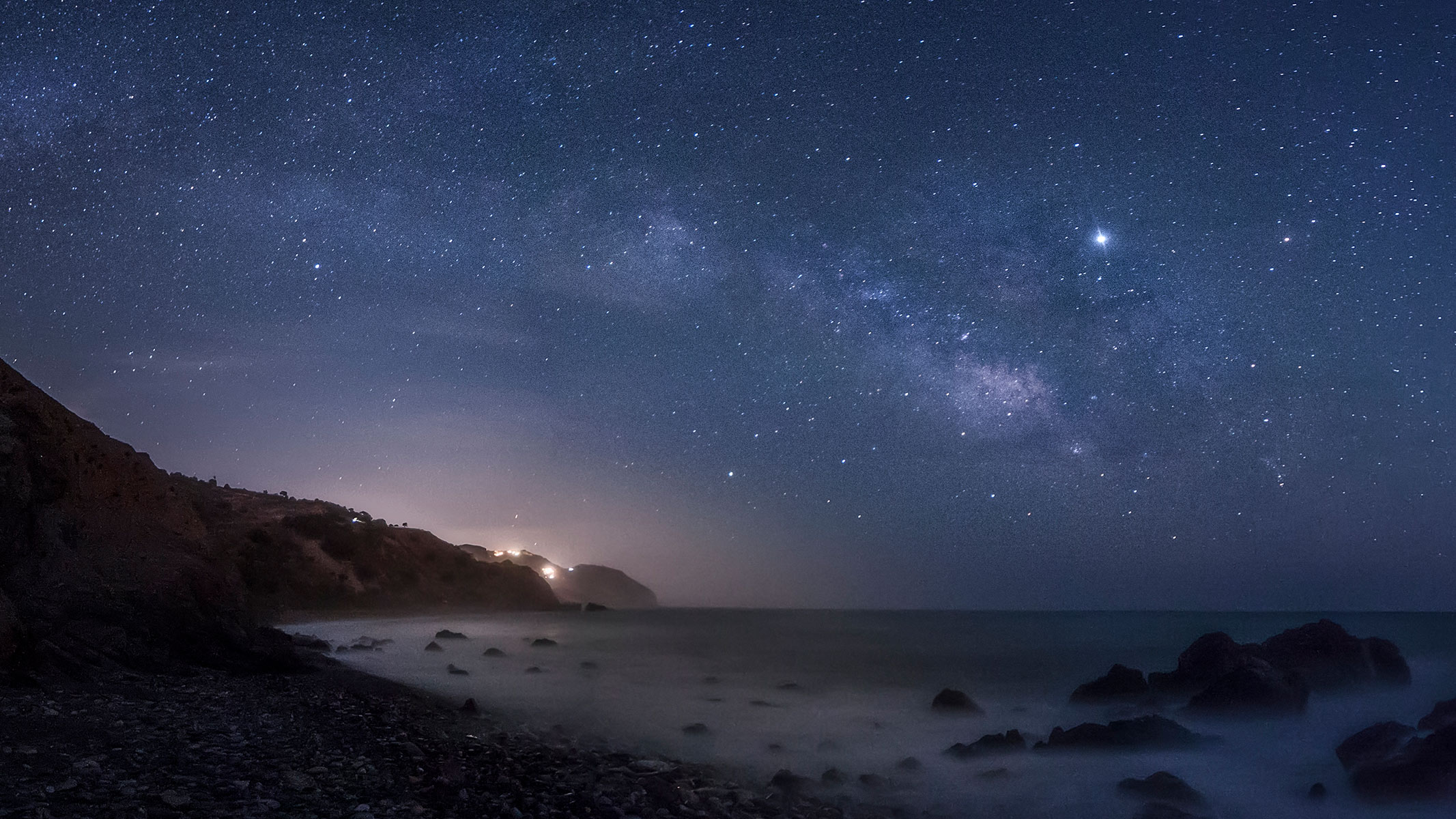 Milky Way stretching over a coast line with many stars and planets visible