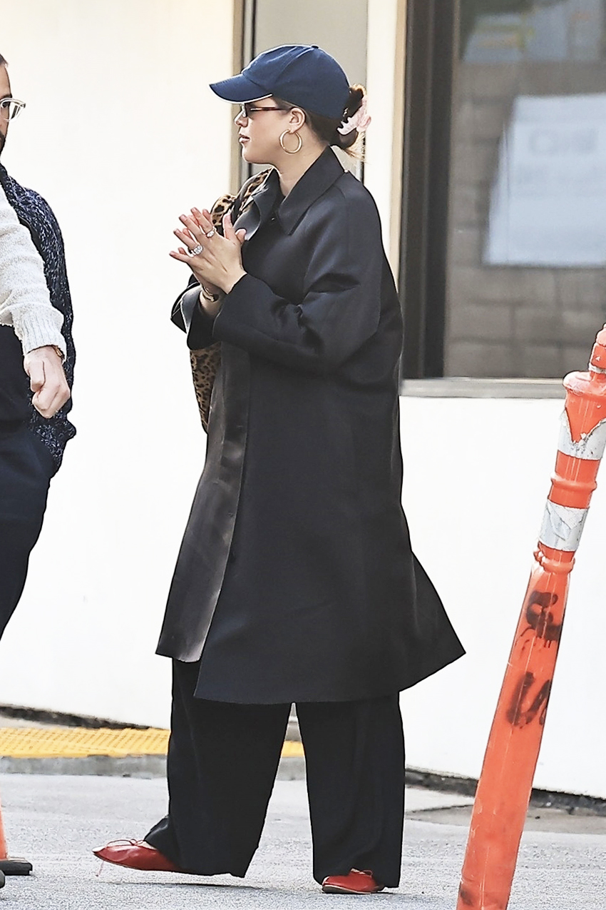 Sofia Richie wearing a black coat, navy baseball hat, black pants, red flats, and a leopard print shoulder bag