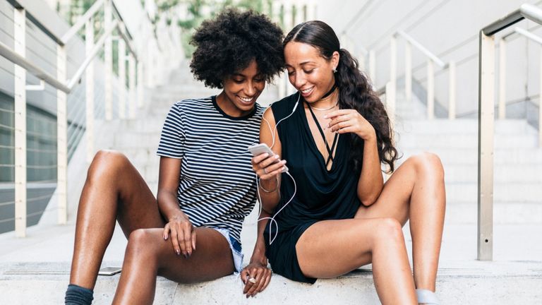 Two friends sitting on stairs listening music together with earphones and smartphone 