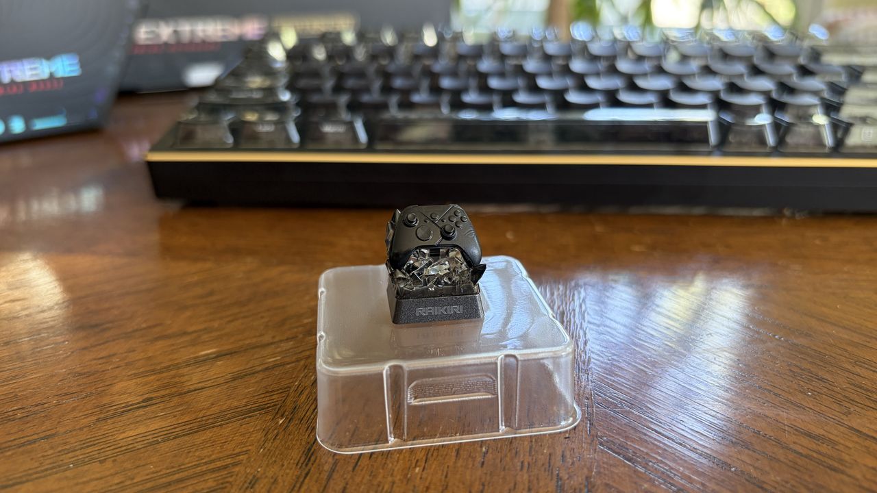 Small black gaming controller keycap on a clear stand labeled "Raikiri," with a keyboard in the background.