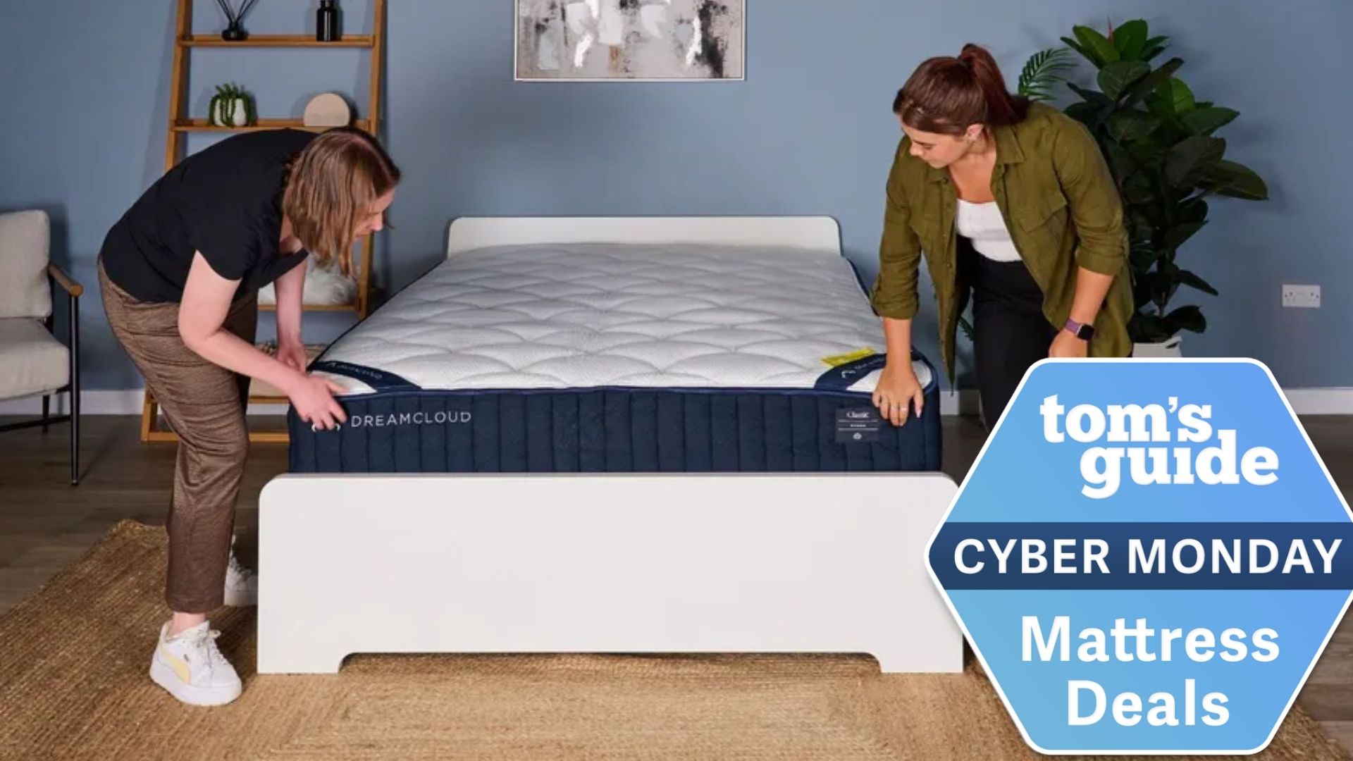 The image shows two women unboxing a navy blue and white mattress, which is placed on a white bed frame against a blue wall. On the top of the image a badge reads &#039;Tom&#039;s Guide Cyber Monday Mattress Deals&#039;
