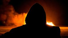 Silhouette of a suspected arsonist in a hoodie in front of a big fire