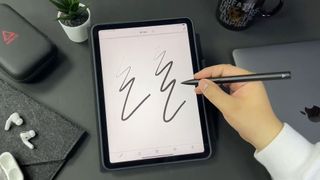 Adonit Note Plus stylus being used by someone to scribble a note. The iPad is placed on an attractive desktop.