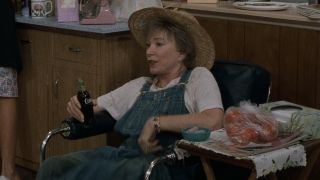 Ouiser sitting in a chair holding a Coke in Steel Magnolias