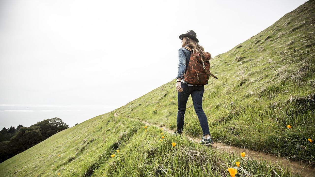 A woman with a backpack and hat on standing at a lookout