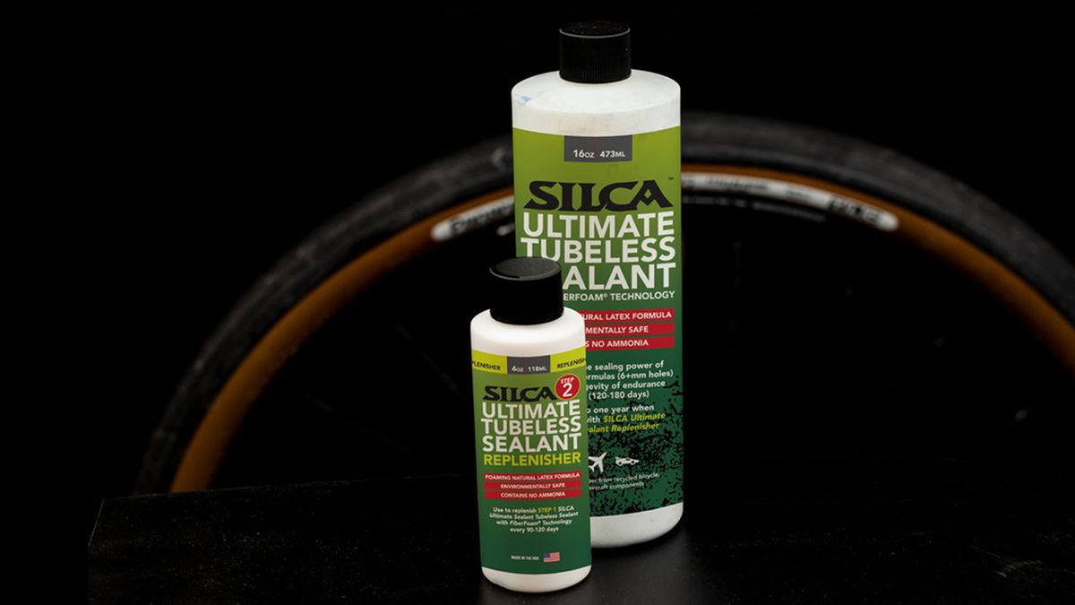 Two white bottles with green labesl stand in front of a tanwall gravel tyre against a black background