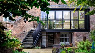 glass extension on rear of property with black framed glass and stairs leading to extension from garden
