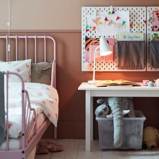 A childrens bedroom with pink walls and a pink metal bedframe