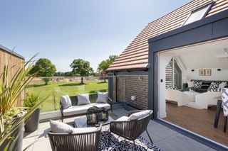 A modern roof terrace overlooking a garden with bifold doors into an open plan kitchen diner