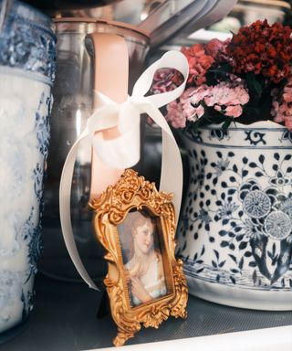 A fridge with a gold picture frame and two blue and white vases filled with purple and pink flowers