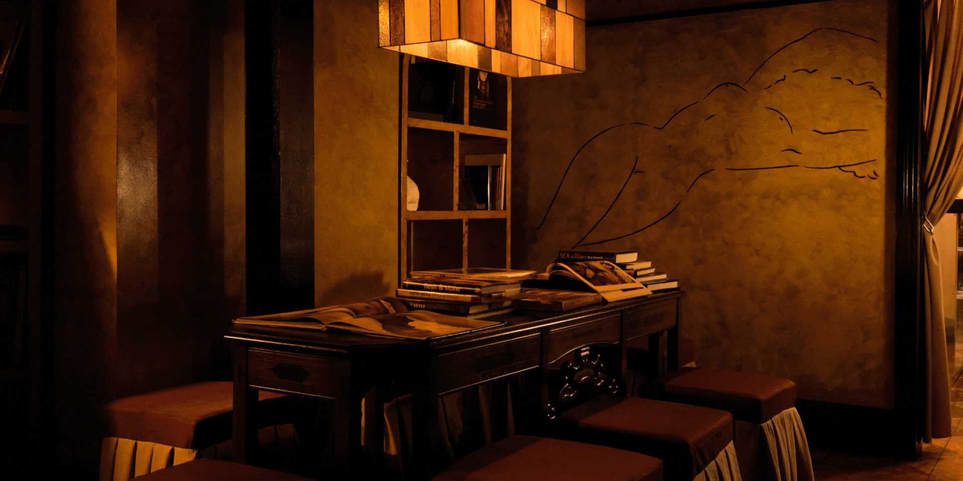 A golden-hued nightclub features a retro-fueled atmosphere punctuated by large scale murals, lantern lighting, marble busts, and reflective chrome surfaces.