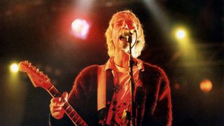 Atmospheric image of Nirvana vocalist Kurt Cobain singing at a microphone and playing guitar in documentary movie 'Kurt Cobain: Moments That Shook Music' 