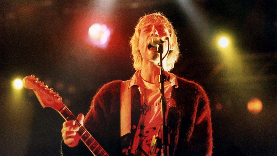 Atmospheric image of Nirvana vocalist Kurt Cobain singing at a microphone and playing guitar in documentary movie &#039;Kurt Cobain: Moments That Shook Music&#039; 