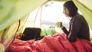 best sleeping bag: A woman drinking a cup of tea in a sleeping bag