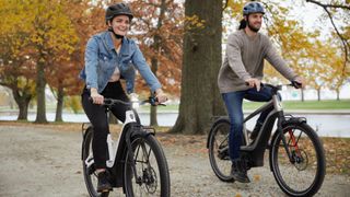 Two people ride Serial 1 e-bikes through a park