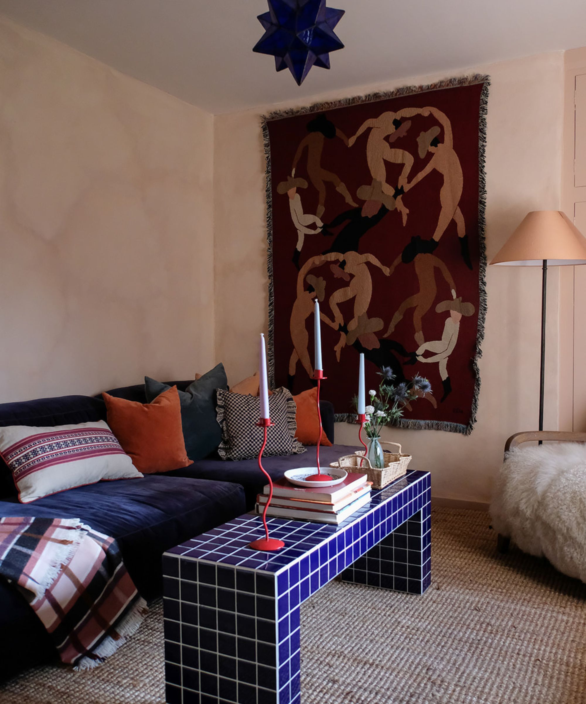 Eclectic living room with pink lime wash walls, tapestry on the wall, blue tiled coffee table, velvet sofa and colourful cushions