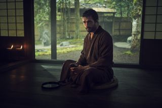 A still from Shogun showing John Blackthorne (Cosmo Jarvis) sitting on the floor in a Japanese house, wearing a robe and holding a cup of tea in his hands
