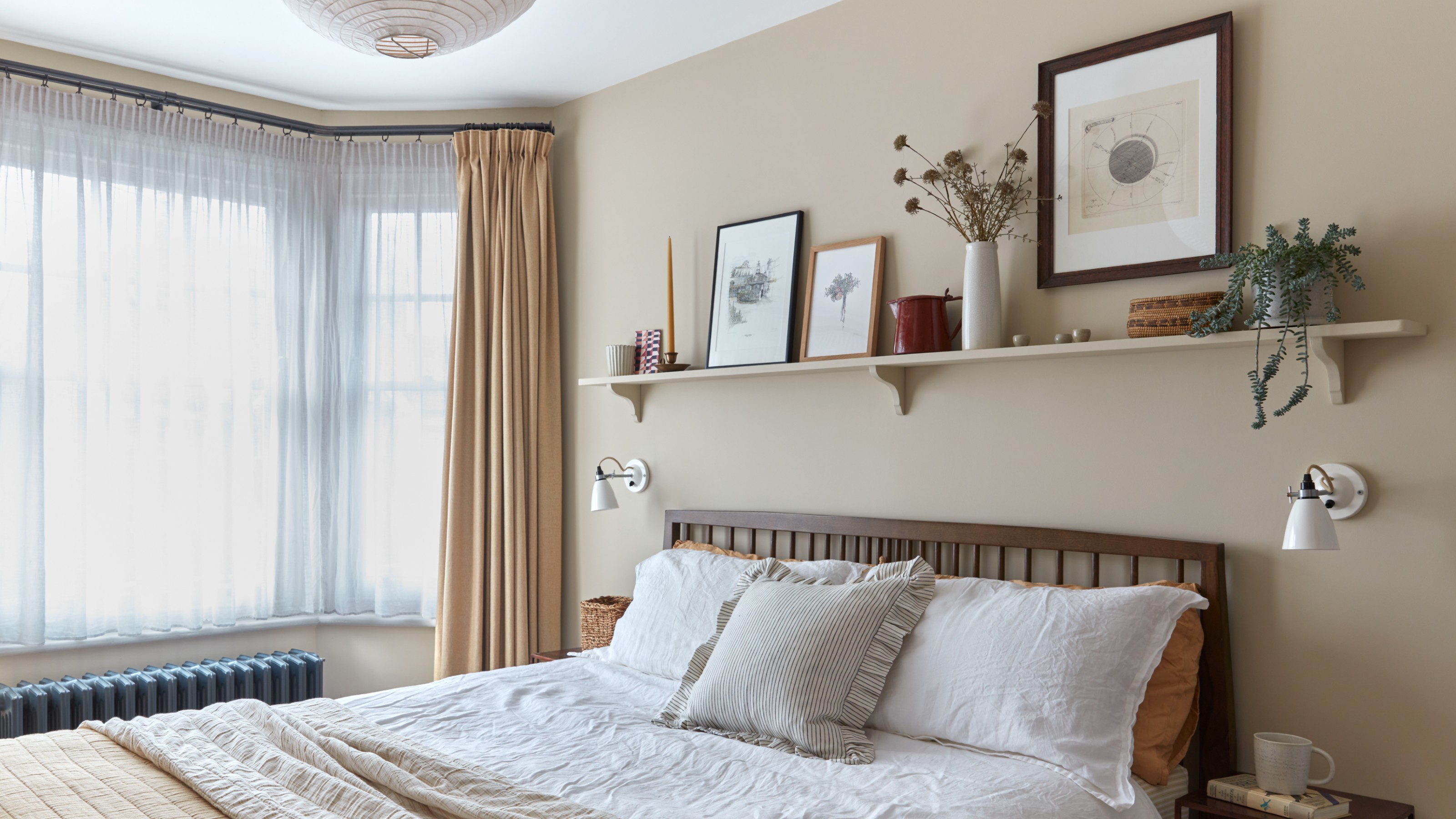 A neutral bedroom with a shelf above the bed displaying framed pictures and decorative objects