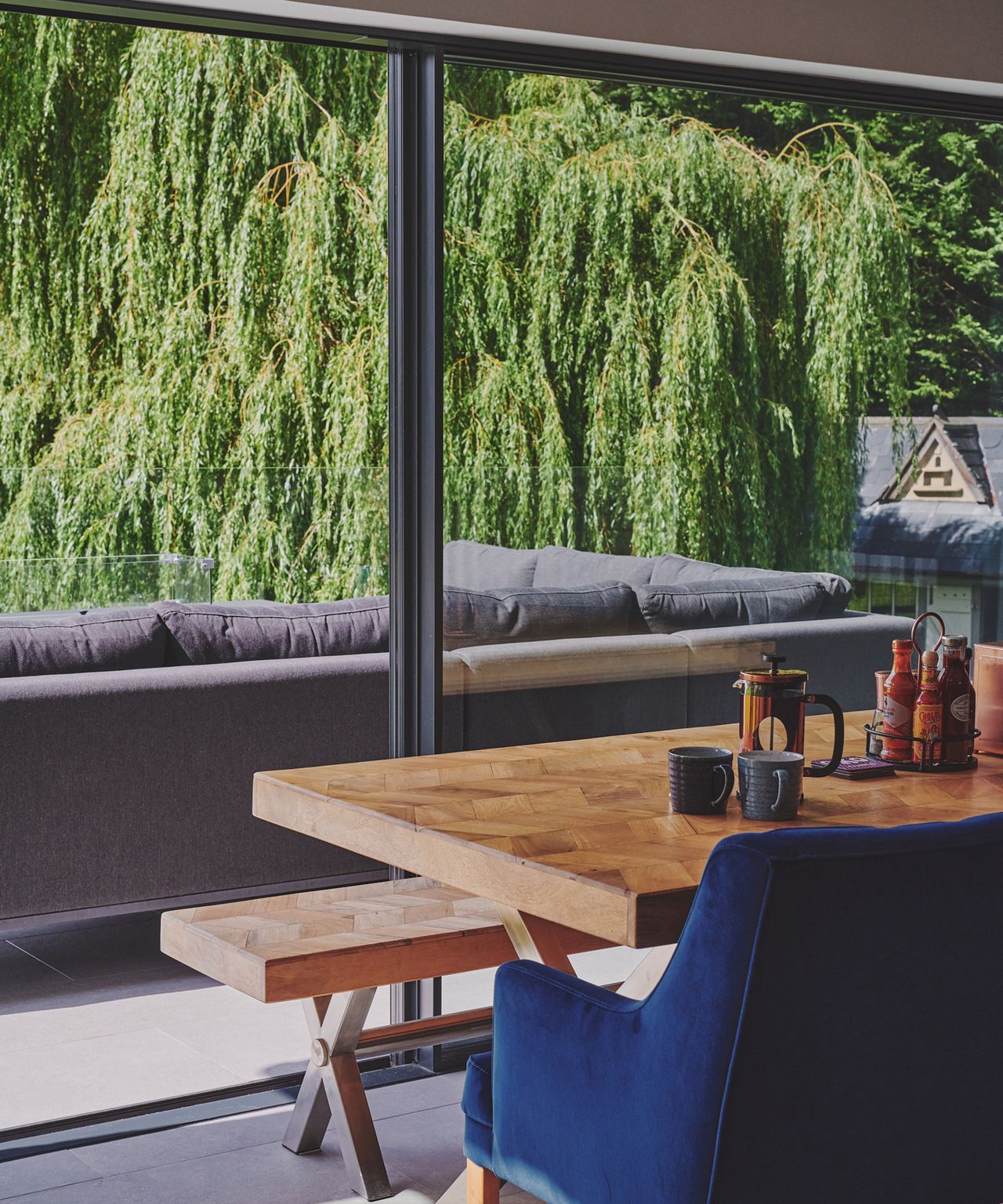 View from a dining table out of large glass sliding doors into a garden patio with willow tree