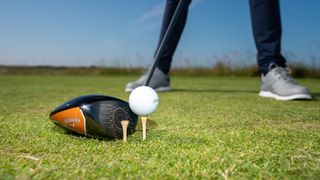 A golf driver lined up with a ball and a tee