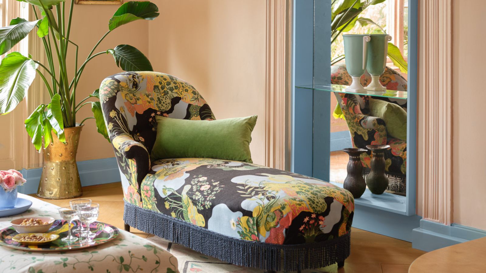 Small living room with colorful lounger and large potted plants. The walls are painted in Benjamin Moore&#039;s Desert View