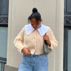 Imani wears cream cardigan, blue jeans, and a green purse