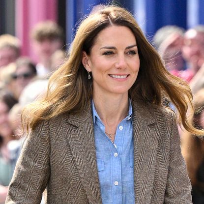 Kate Middleton wearing a blue shirt and brown blazer smiling