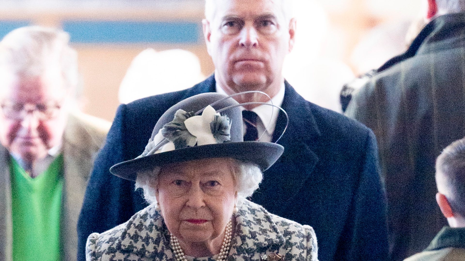 Queen Elizabeth wears a white and black jacket and her son ex-Prince Andrew looks stern in the background