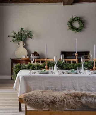 A simple rustic dining table with green garland and candlesticks