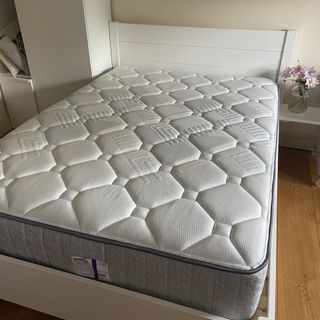 The Sealy Newton Posturepedic Mattress being tested in a bedroom with a white bed frame and wooden floor