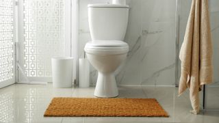 A toilet with a yellow toilet mat in front