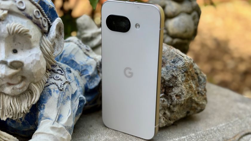 The porcelain Google Pixel 9a sitting on a bench next to a gnome.