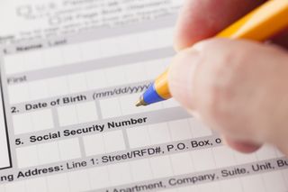 Social security number fields in application form and human hand with ballpoint pen.