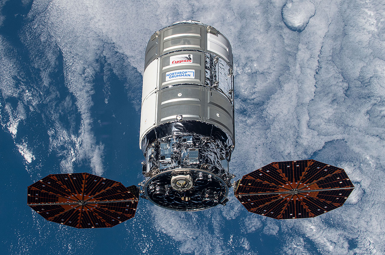 cylindrical spacecraft with two solar panels attached, with earth as backdrop