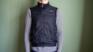 A man wearing a black Assos Tactica gilet over a grey long sleeve shirt