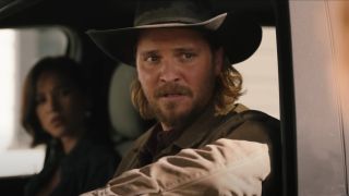 Luke Grimes as Kayce in Yellowstone. He's sitting in his truck looking out the window.