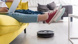 Cropped view of kid with laptop near mother with raised legs on sofa and robotic vacuum cleaner on floor in living room