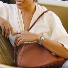 Woman in leather car seat wearing silver Fossil square-face watch and brown Fossil leather bag.