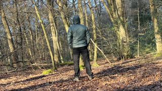 Hiker wearing Helly Hansen Odin Everdown hooded jacket in the woods - back view