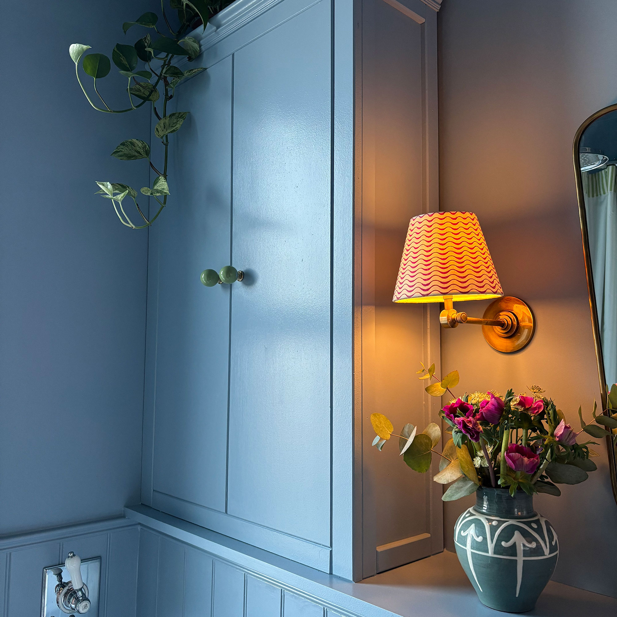 Brass wall light with red and white patterned shade beside built-in cabinetry in blue bathroom