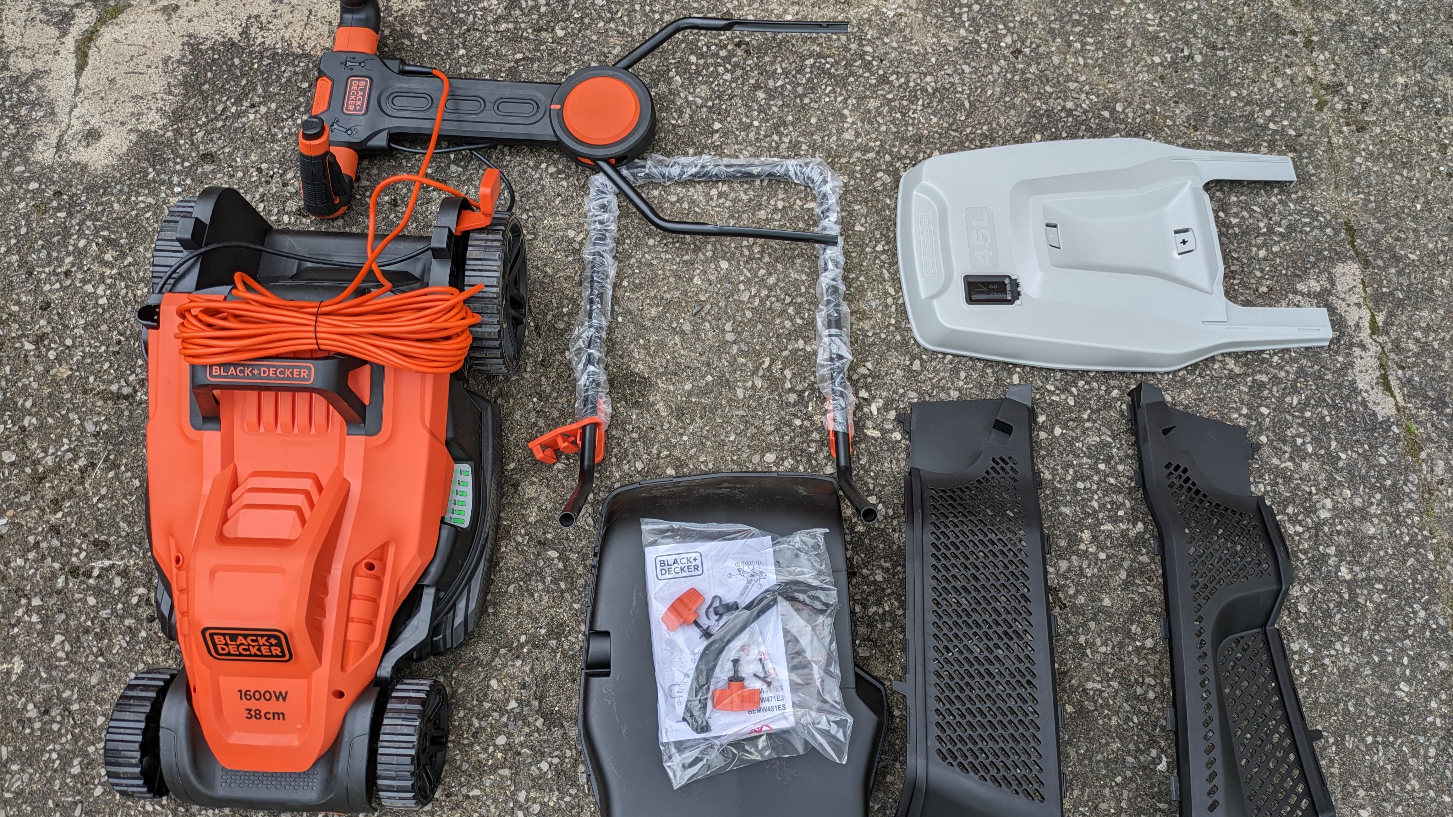 The flat-packed components of the Black and Decker lawnmower, spread out on the ground after unboxing.