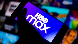 HBO Max logo on a phone, held by a hand in front of a grid of pictures