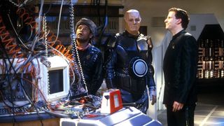 Still from the British sci-fi sitcom called Red Dwarf. From 'The White Hole' episode, here we see Lister, Kryten, and Rimmer standing in front of a complicated looking computer terminal with a lot of wires.