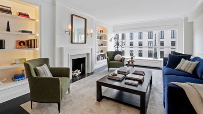 living room in white with blue sofa, 2 green armchairs, fireplace and bookshelves left and right of fireplace 